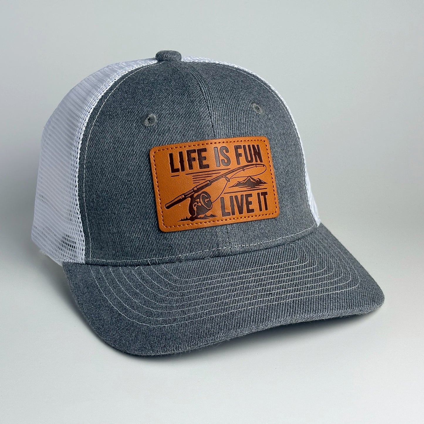 Grey and white mesh trucker hat with Life Is Fun Live It leather patch front view